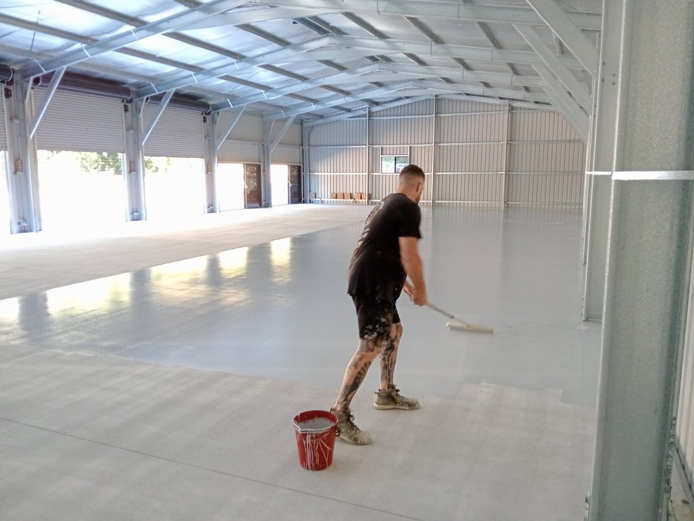 Tori Faux of Epoxy Armour Coatings squeegeeing a base coat across a commercial shed floor